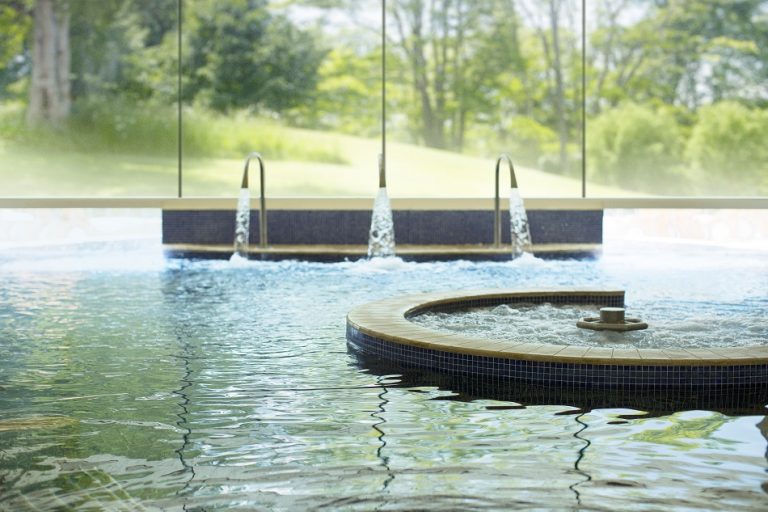 Outdoor hydrotherapy pool at Aquarias Spa Whatley Manor illuminated at twilight with bubbling recliners