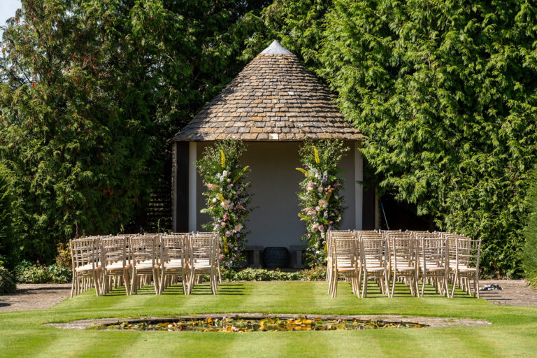 Lush green lawns of Whatley Manor framed by Cotswold stone gazebo and herbaceous border plantings